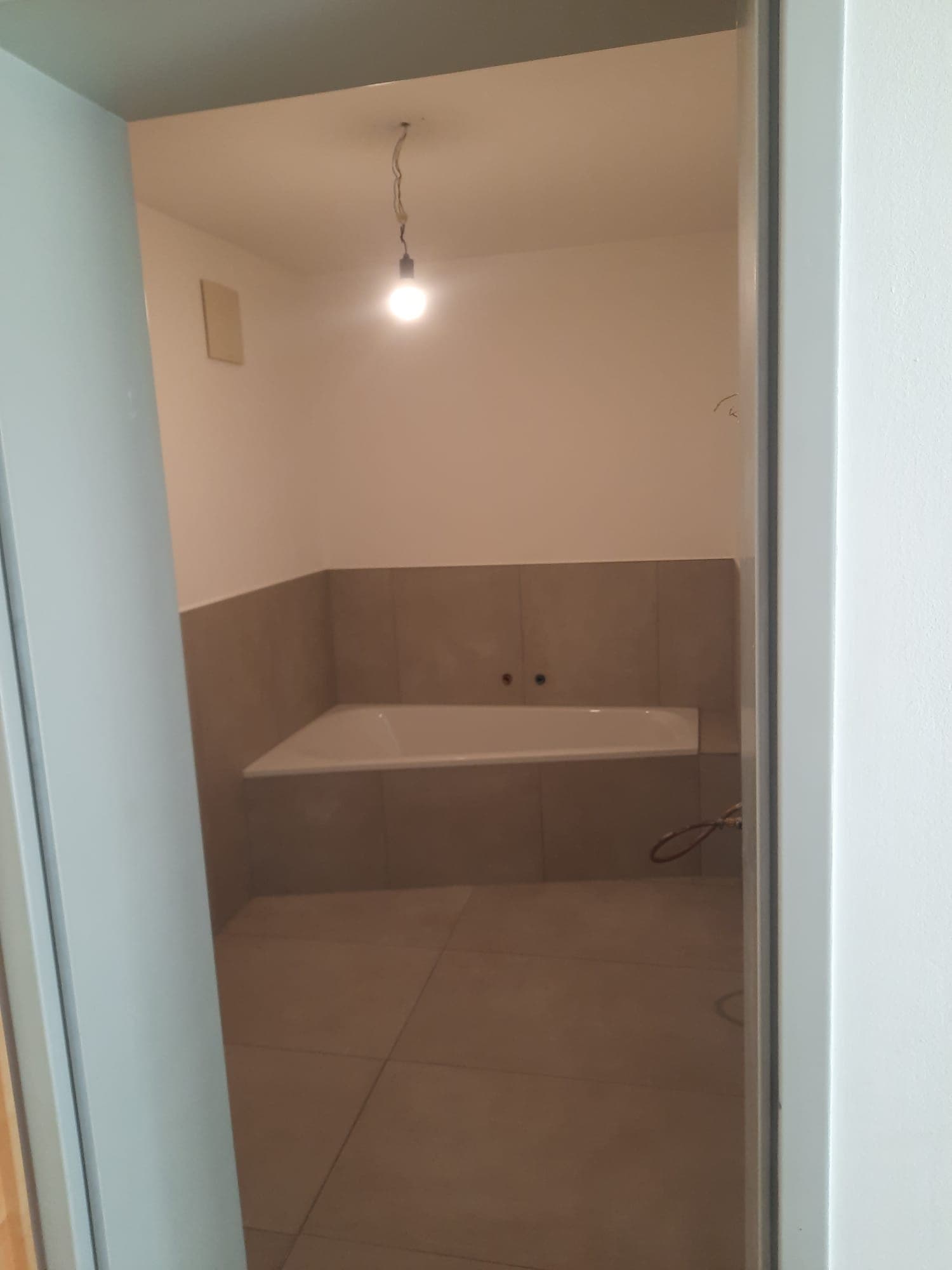 Professionell verlegte Eckbadewanne mit modernen Großformatfliesen in Schieferoptik