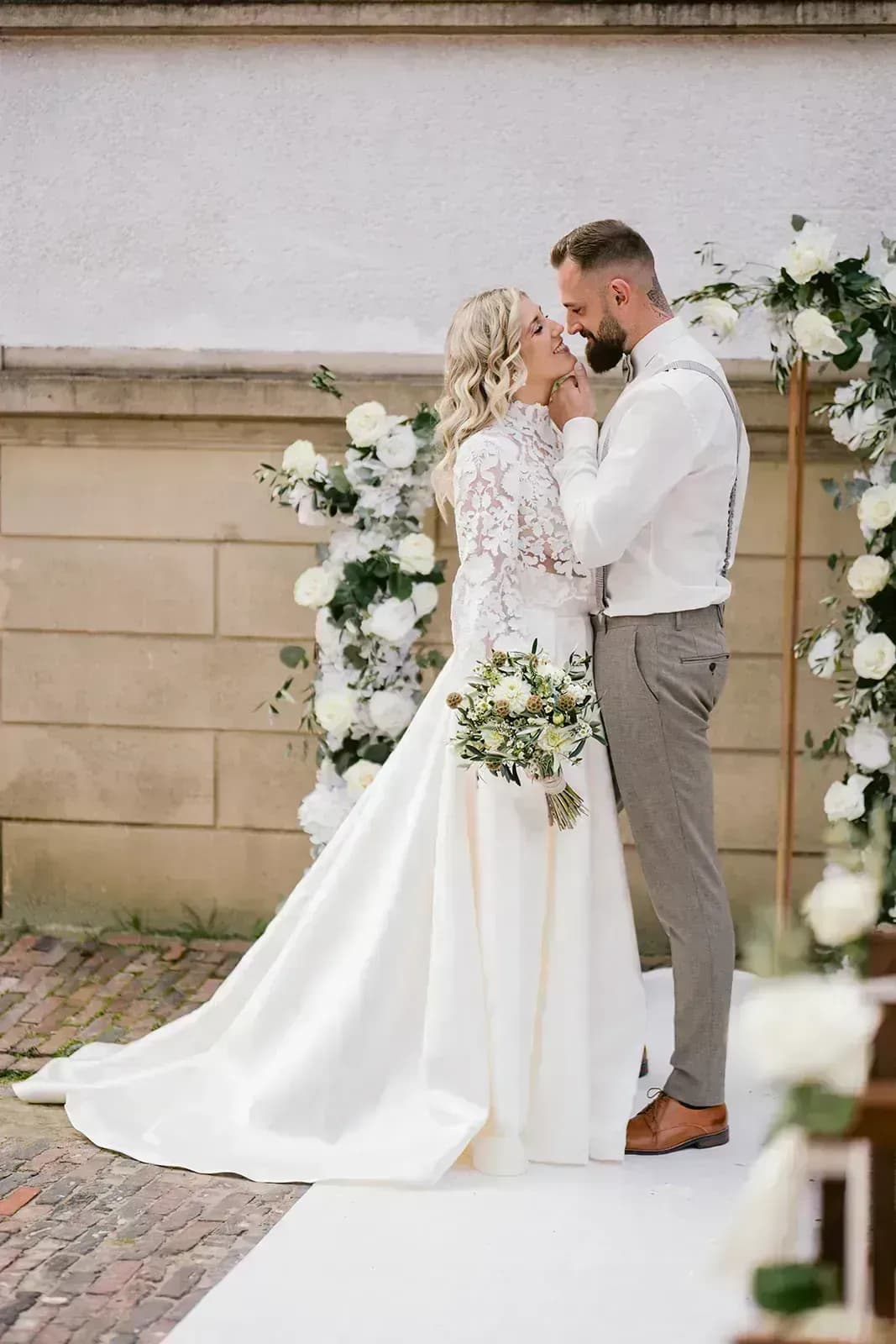 Glückliches Brautpaar entspannt bei ihrer Hochzeitstafel, während im Hintergrund ein Fotograf arbeitet – perfekte Planung trotz kurzfristigem Ausfall eines Dienstleisters.