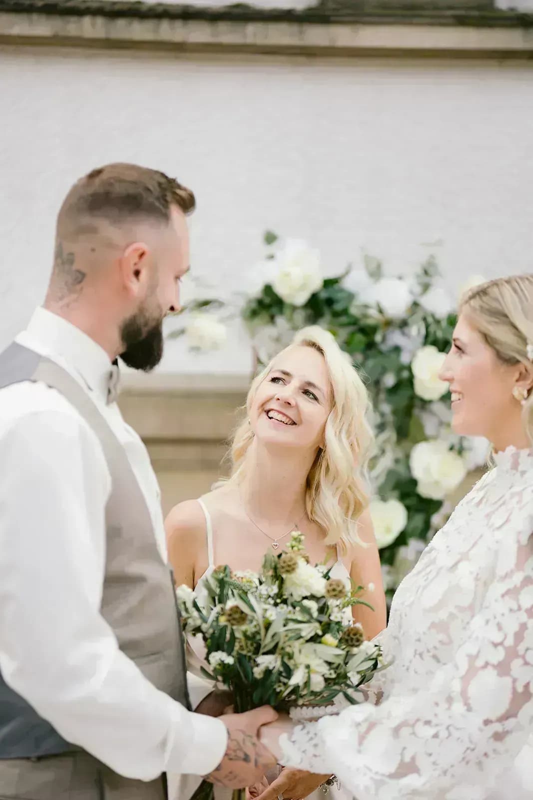 Glückliches Brautpaar entspannt bei ihrer Hochzeitstafel, während im Hintergrund ein Fotograf arbeitet – perfekte Planung trotz kurzfristigem Ausfall eines Dienstleisters.
