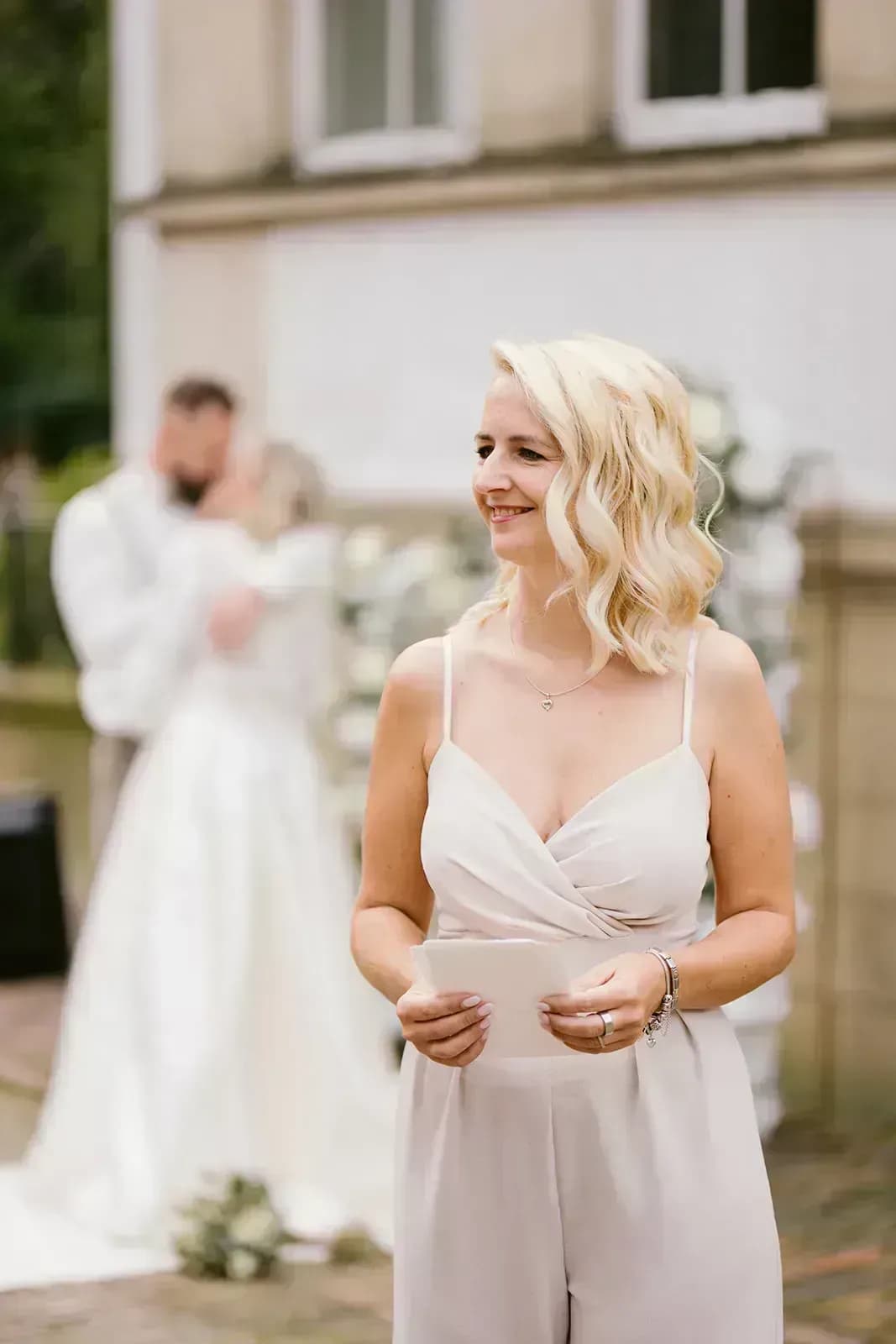 Glückliches Brautpaar entspannt bei ihrer Hochzeitstafel, während im Hintergrund ein Fotograf arbeitet – perfekte Planung trotz kurzfristigem Ausfall eines Dienstleisters.